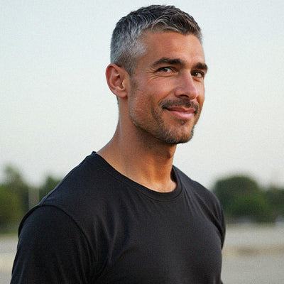 Man with gray hair wearing a black shirt outdoors smilimg at camera.