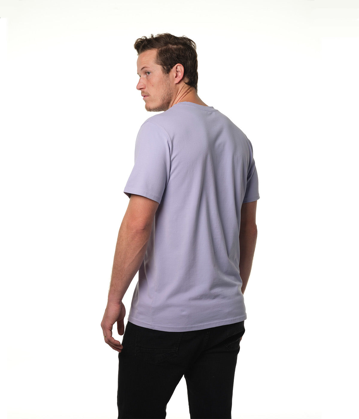 Male model turned partially away from camera looking back over left shoulder wearing our "lilac sky" light purple t-shirt