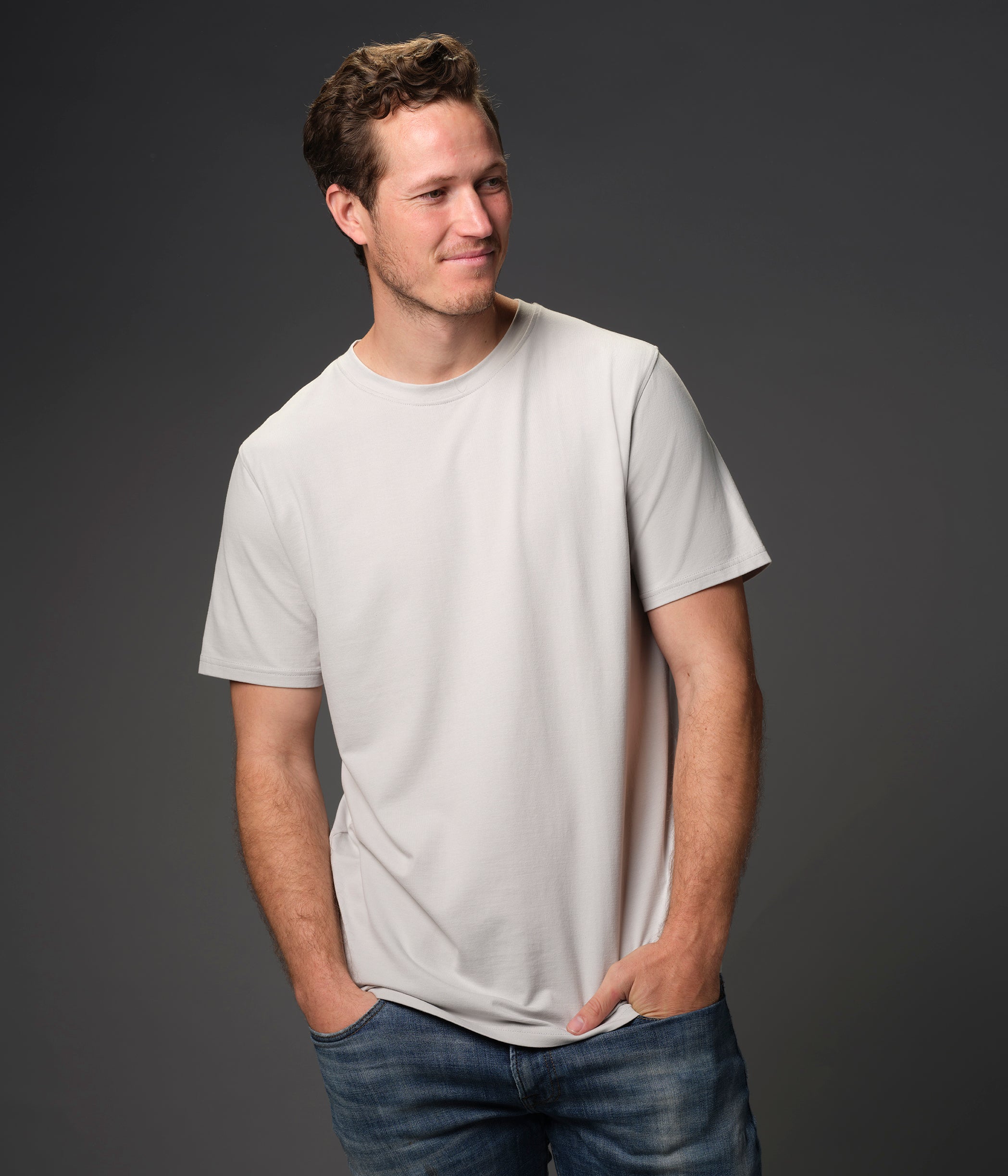 Male model grinning looking to right wearing our "ash" gray premium t-shirt dark background