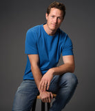 Male model seated on stool wearing our “azure" blue t-shirt dark background