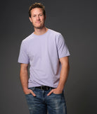 Male model wearing partially tucked in "lilac sky" light purple t-shirt dark background